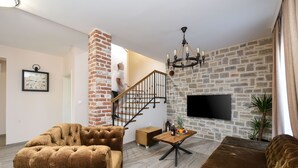 A modern living room with a brick column, a staircase, a chandelier, a flat-screen TV, and a sofa. - Villa Imperia ZadarVillas (Pridraga)