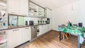 A modern kitchen with white cabinets, a stainless steel dishwasher, and a dining area with a table set for two. - Maisonette Bad Camberg (Bad Camberg)