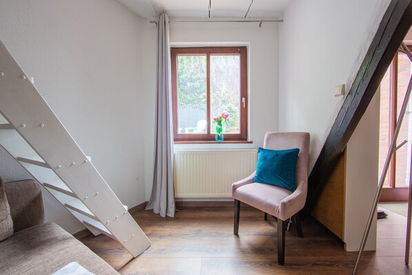 Une pièce avec un plancher en bois, une fenêtre donnant sur un beau paysage, une chaise avec un coussin et un radiateur blanc.