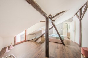 Ein geräumiges Schlafzimmer im Dachgeschoss mit geneigter Decke, Holzbalken und einem großen Fenster, das für natürliches Licht sorgt.