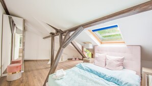 A bedroom with a sloped ceiling, a skylight, a bed with pink and blue bedding, and a wooden floor. - Maisonette Bad Camberg (Bad Camberg)