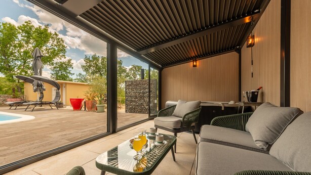 Un espacio exterior moderno con piscina, sillones de descanso y una mesa de vidrio con comida para el desayuno.