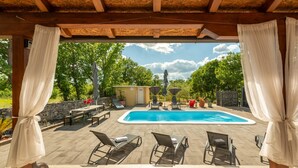 Un área de piscina al aire libre con sillones de descanso, un pequeño edificio y un muro de piedra.