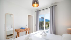 A hotel room with two beds, a wooden desk, a mirror, and a view of the outdoors. - Villa Katerina Mentoros (Kefalonia)