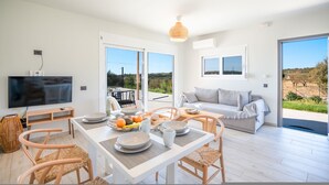 A modern living room with a dining area, large windows, and a view of the outdoors. - Villa Katerina Mentoros (Kefalonia)