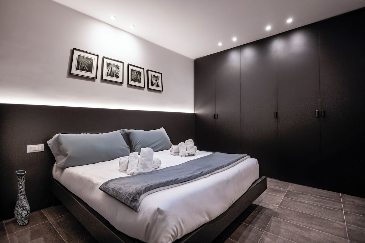 Une chambre à coucher moderne avec un grand lit, des murs de couleur sombre et une armoire intégrée.