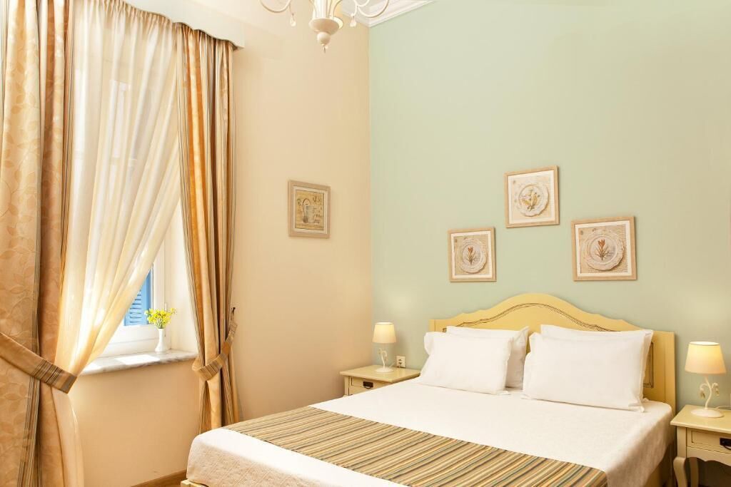 A hotel room with a bed, two bedside tables, a window with curtains, and wall-mounted artwork.