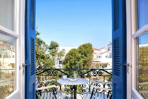 An open balcony with a table set for two, overlooking a residential area with trees and buildings. - Egli Hotel (Andros)