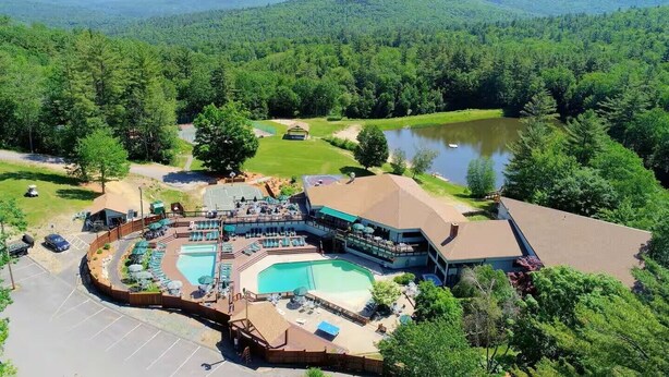 A resort with a large pool, outdoor seating, and a view of the surrounding forest and mountains.