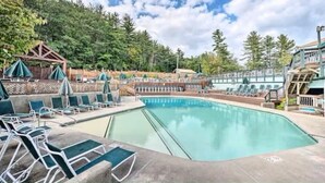 A swimming pool with lounge chairs and umbrellas, surrounded by trees and a wooden deck.