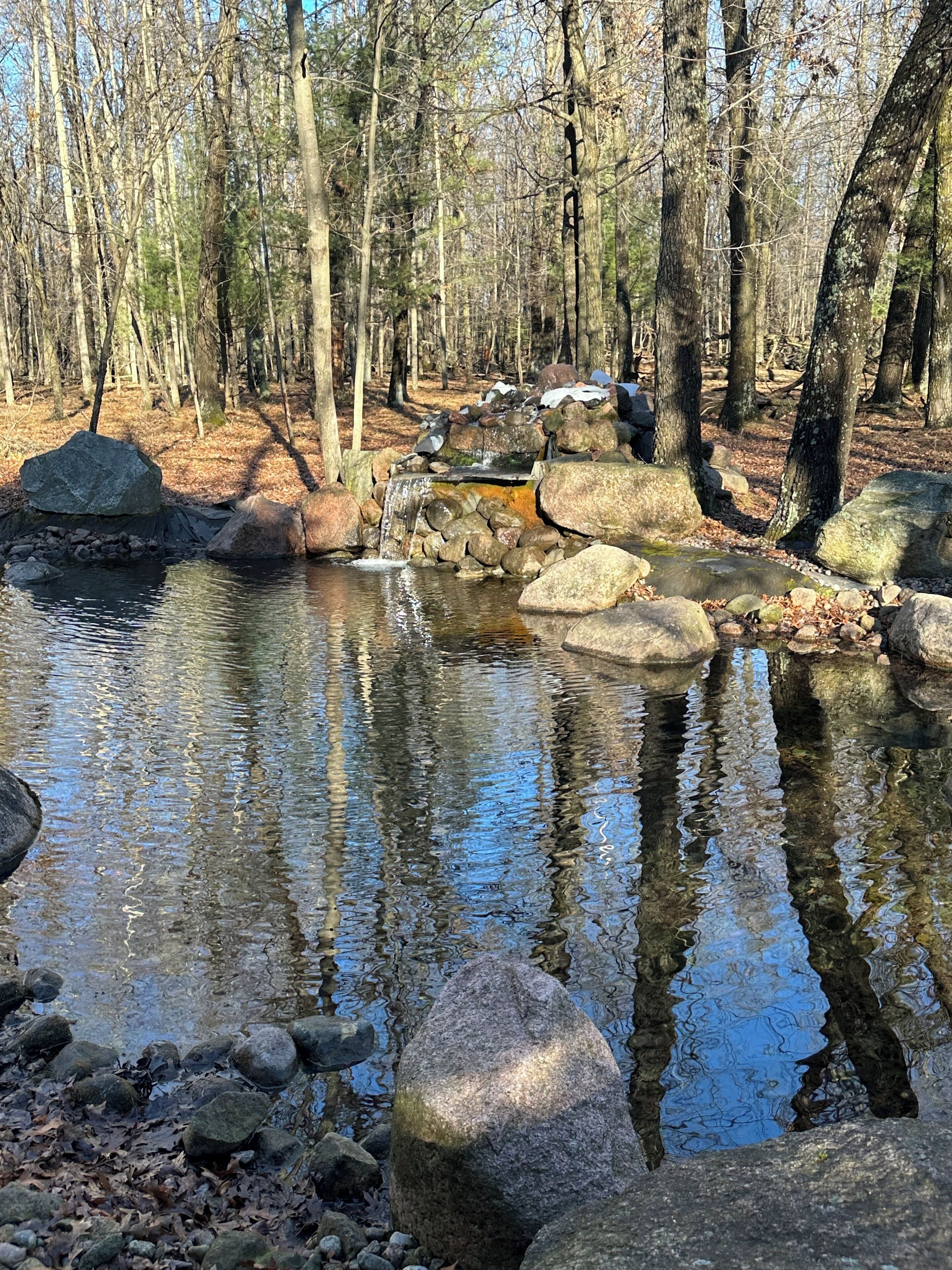 A natural outdoor setting with a small stream, surrounded by rocks and trees.
