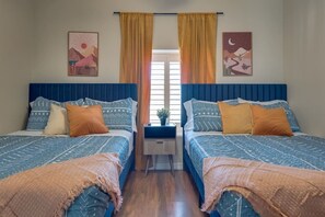 Une chambre avec deux lits, chacun agrémenté de draps à motifs et de têtes de lit assorties. Il y a une table de chevet entre les lits et une fenêtre avec des rideaux.