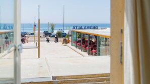A view from a window overlooking a beachside area with a café and outdoor seating. - Casa da Praça (Sesimbra)