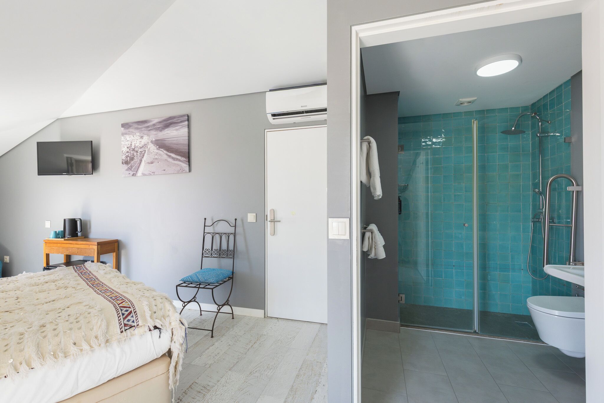 A bedroom with a bed, a chair, a television, and a wall-mounted air conditioner.