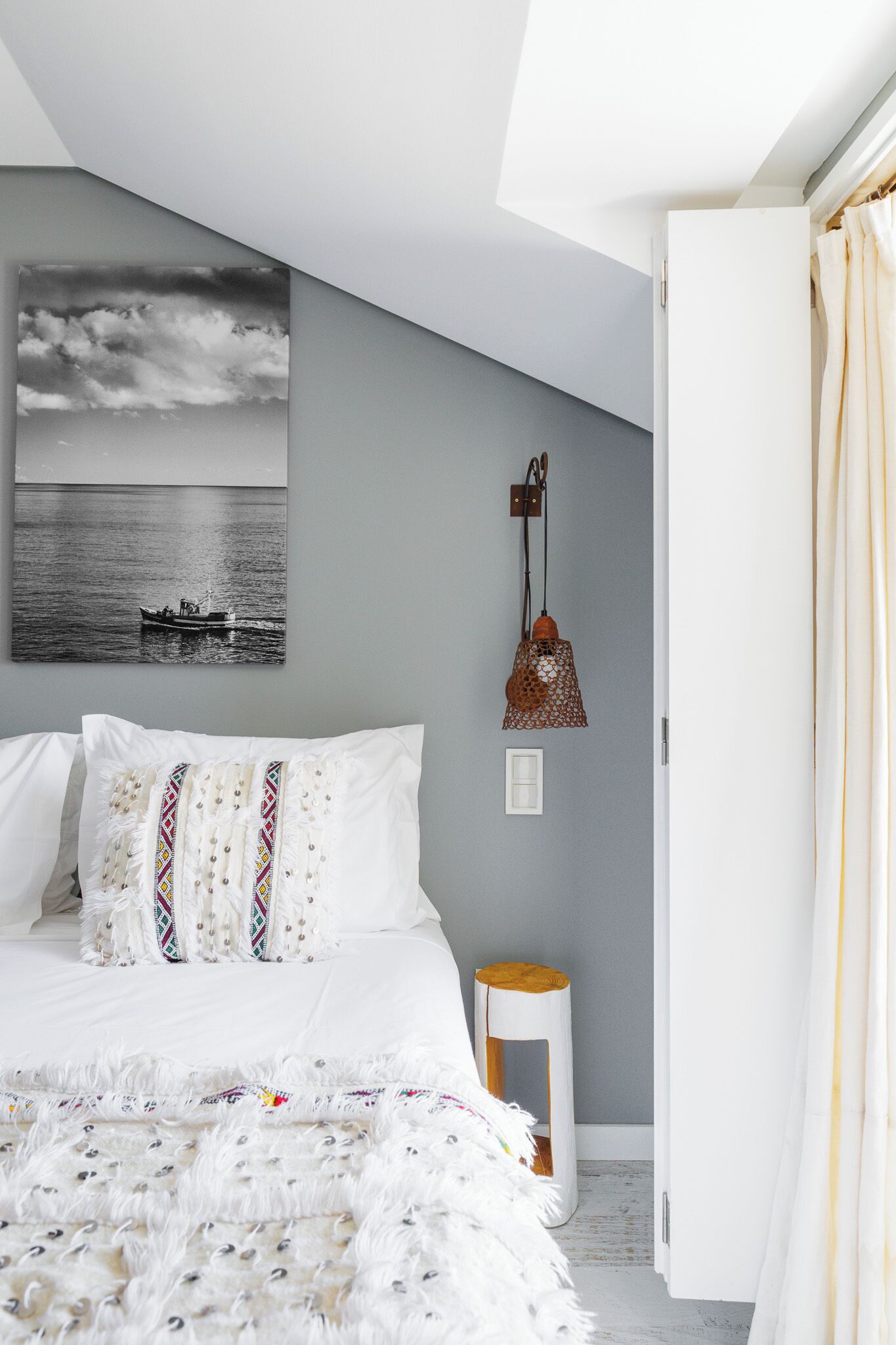 A bedroom with a bed, a wall-mounted lamp, and a painting of a boat on the wall.