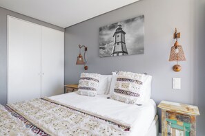 A bedroom with a bed, a painting of a lighthouse, a hanging lamp, and a small table. - Casa da Praça (Sesimbra)