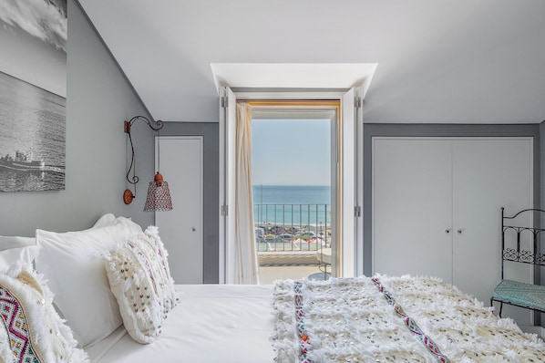Een slaapkamer met een bed, uitzicht op zee, een balkon en een deur.