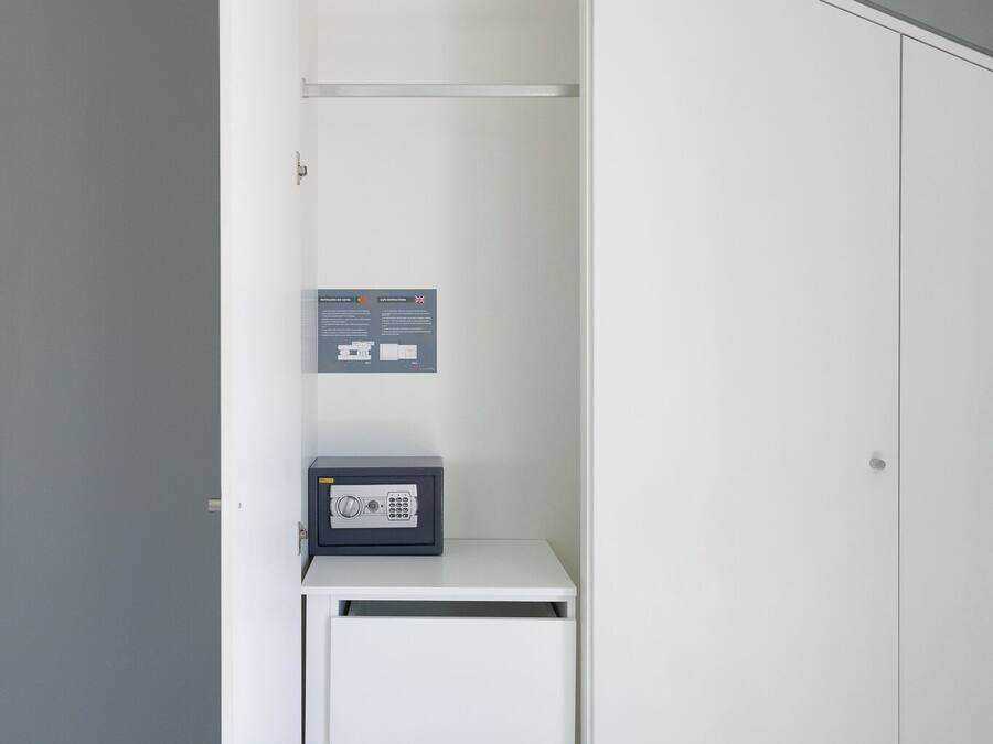 A walk-in closet with a white wardrobe, a small safe, and a wall-mounted instruction panel.