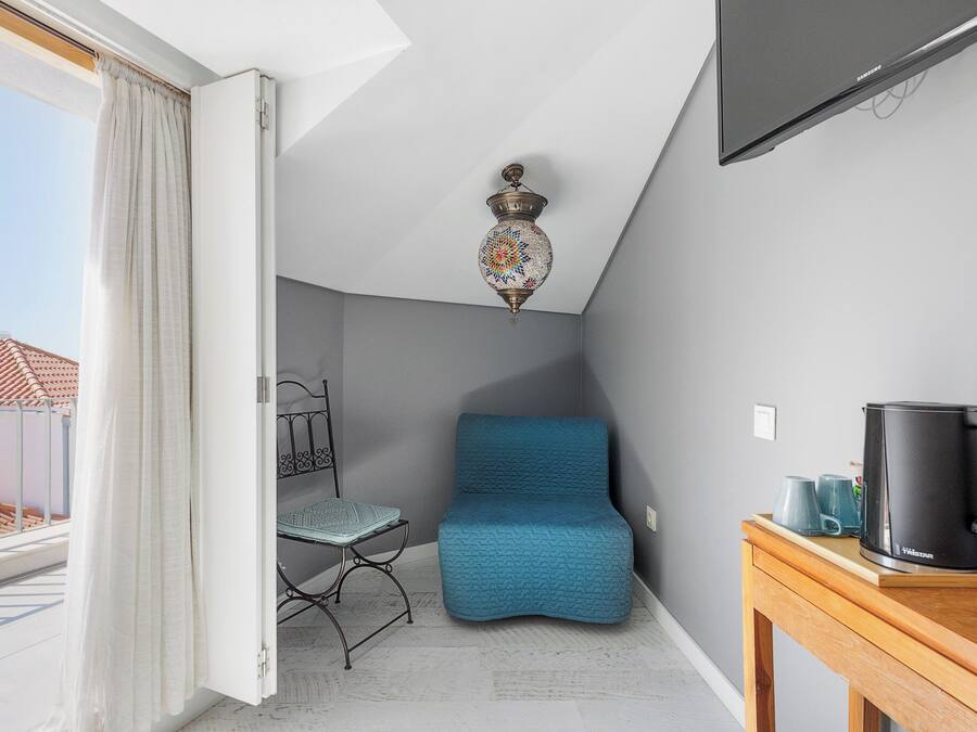 A room with a blue sofa, a small table with a black coffee maker, a metal chair, and a ceiling light fixture.