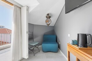 A room with a blue sofa, a small table with a black coffee maker, a metal chair, and a ceiling light fixture. - Casa da Praça (Sesimbra)