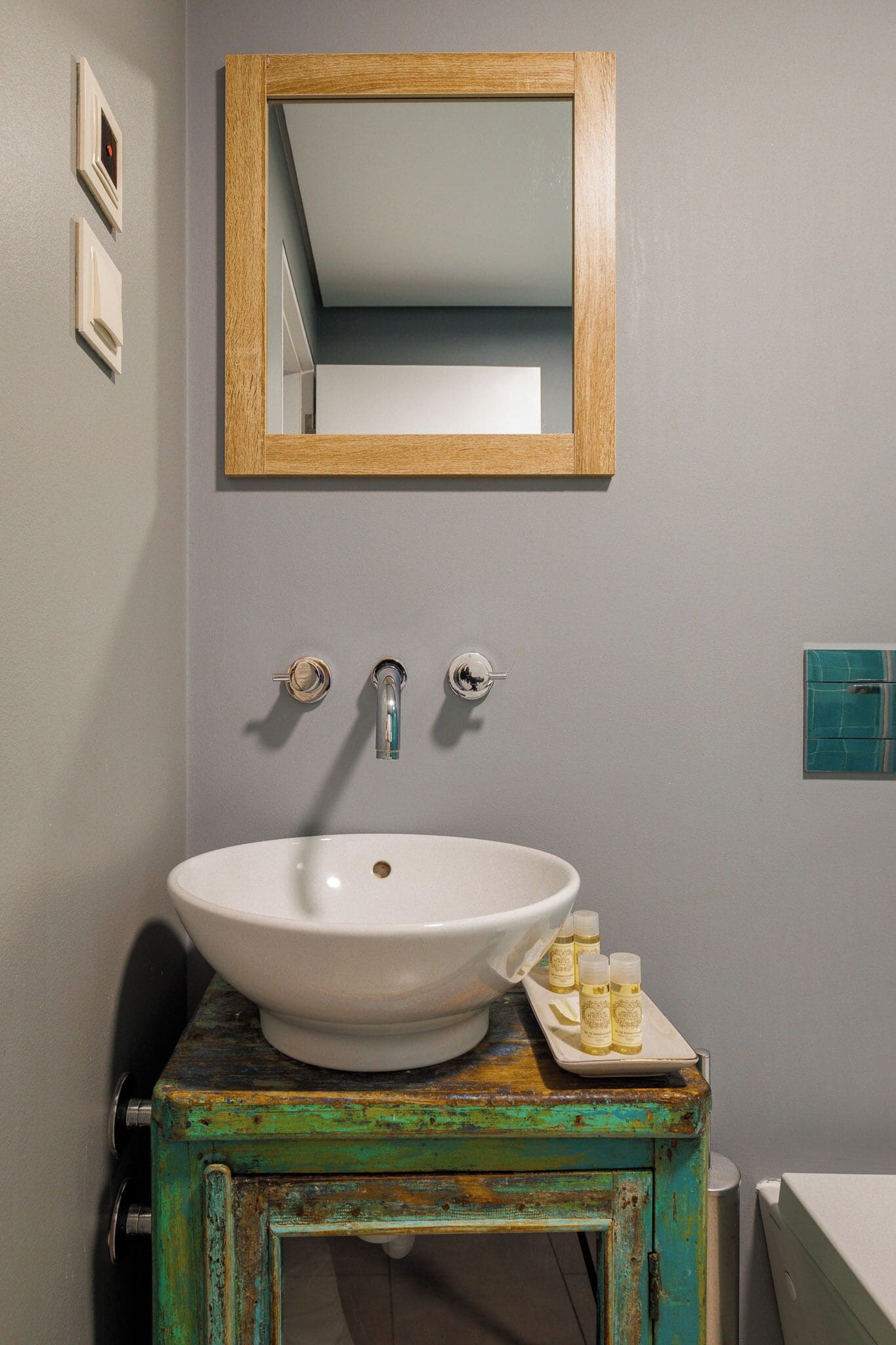 Un baño con un lavamanos blanco, un espejo con marco de madera y un estante con artículos de aseo.