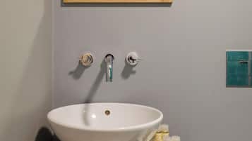 A bathroom with a white sink, a wooden-framed mirror, and a small shelf with toiletries.