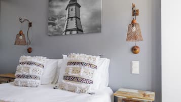 A bedroom with a bed, a wall-mounted lamp, a picture of a lighthouse, and a small wooden nightstand.