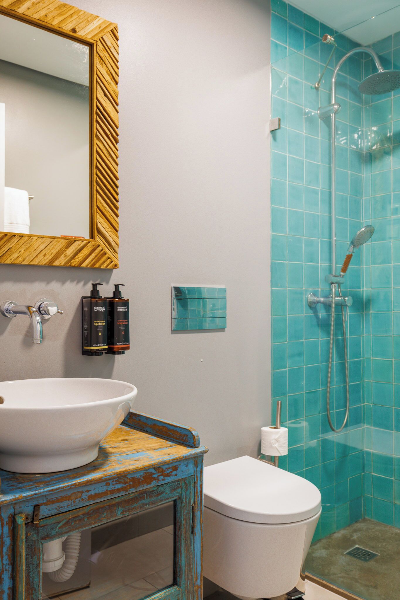 Un baño con un lavabo blanco, un espejo con marco de madera, un inodoro y una ducha con azulejos azules.
