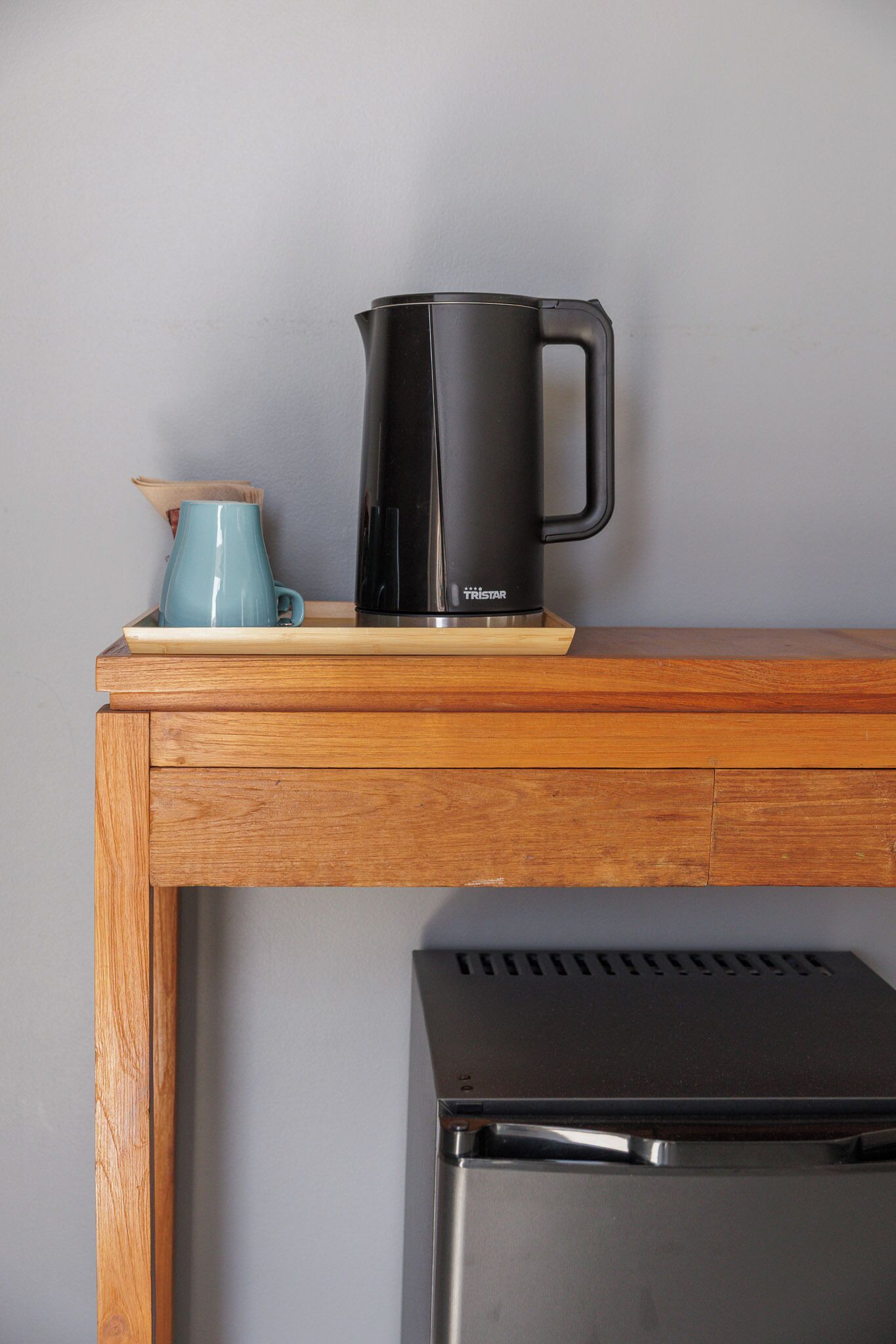 A black coffee maker on a wooden table with a blue mug beside it.