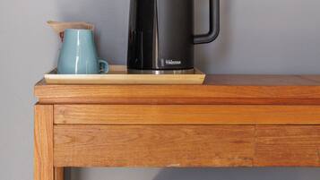 A black coffee maker on a wooden table with a blue mug beside it.