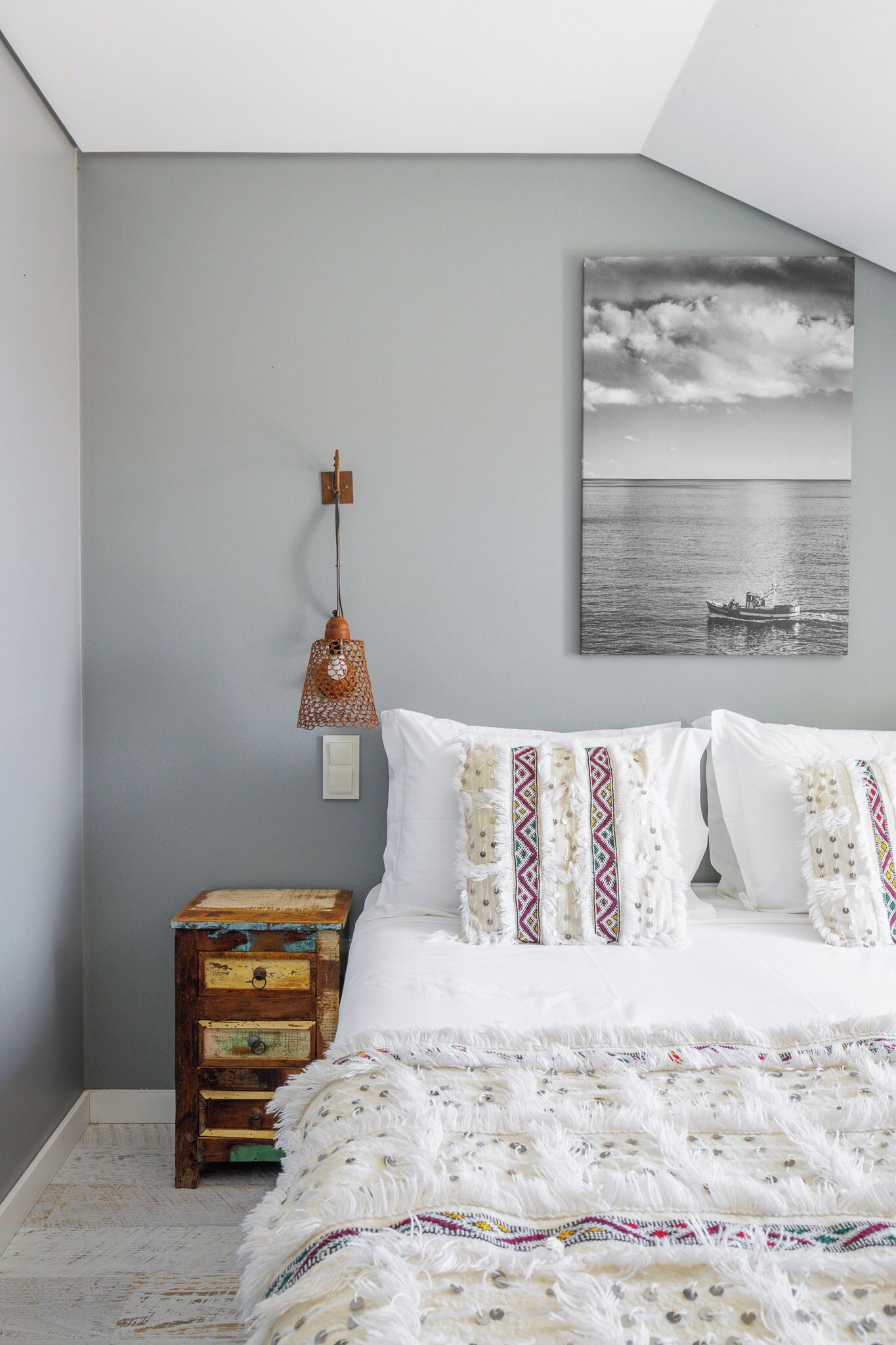 Un dormitorio con cama, mesita de noche, lámpara de pared y un cuadro enmarcado.