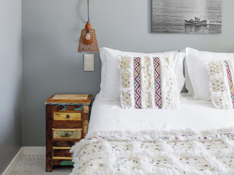 A bedroom with a bed, a nightstand, a wall-mounted lamp, and a framed picture.