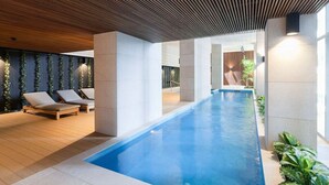 Un espace piscine intérieur moderne, doté de chaises longues et d’un long bassin.