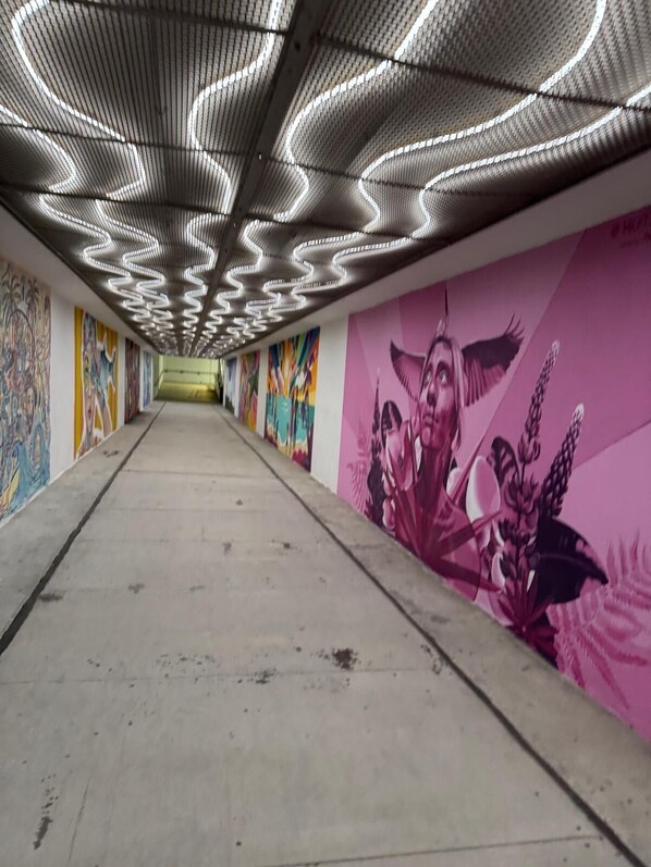 Un pasillo interior con techo estampado, murales coloridos en las paredes y suelo de concreto.