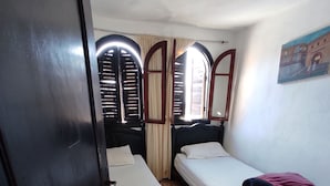 Ein kleiner, kompakter Raum mit zwei Einzelbetten, einem Kleiderschrank und einem Fenster mit Rollläden.