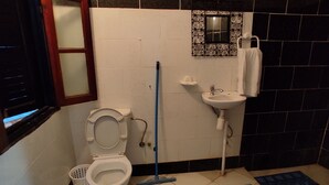 A small bathroom with a toilet, a sink, a mirror, and a mop. - CASA DAOUED APRT C (CHEFCHAOUEN)