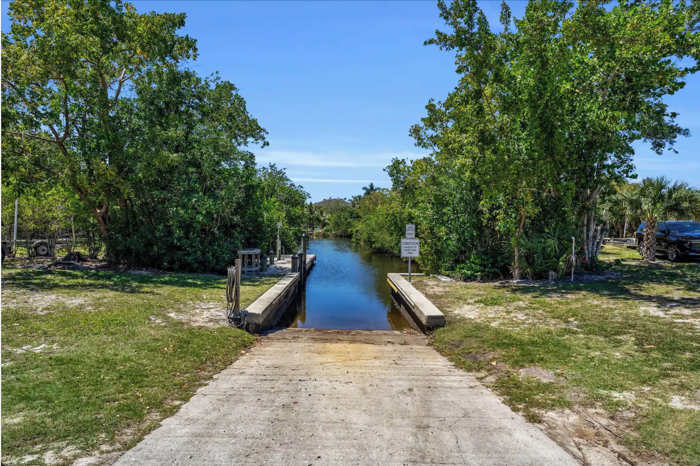 A concrete pathway leading to a canal flanked by lush green trees.