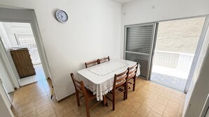Een eetruimte met een tafel en stoelen, een klok aan de muur en een schuifdeur naar een buitenbalkon.