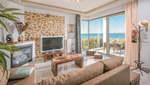 A living room with a stone wall, a fireplace, a television, and a view of the sea.