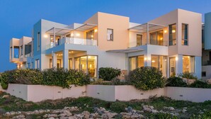 A modern multi-story building with balconies, large windows, and a landscaped garden with rocks and shrubs.