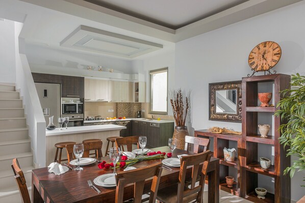 A modern kitchen with a central island, a dining area with wooden furniture, and a decorative clock on the wall.