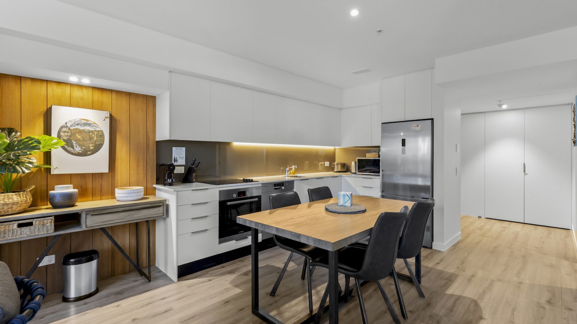 Une cuisine moderne avec des meubles blancs, une table à manger en bois et un réfrigérateur en acier inoxydable.