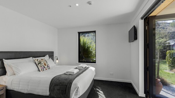 Camera da letto moderna con un letto grande, una finestra vista su spazi verdi e una TV a schermo piatto montata a parete.