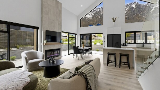 A modern living room with a fireplace, a dining area, and a kitchen with a large window overlooking mountains. - Marvellous on Muster - family home, mountain views (Jacks Point)