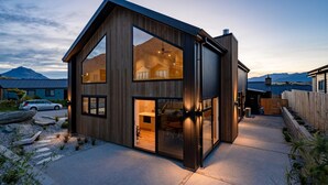 A modern two-story house with large windows, a visible kitchen area, and a driveway. - Marvellous on Muster - family home, mountain views (Jacks Point)