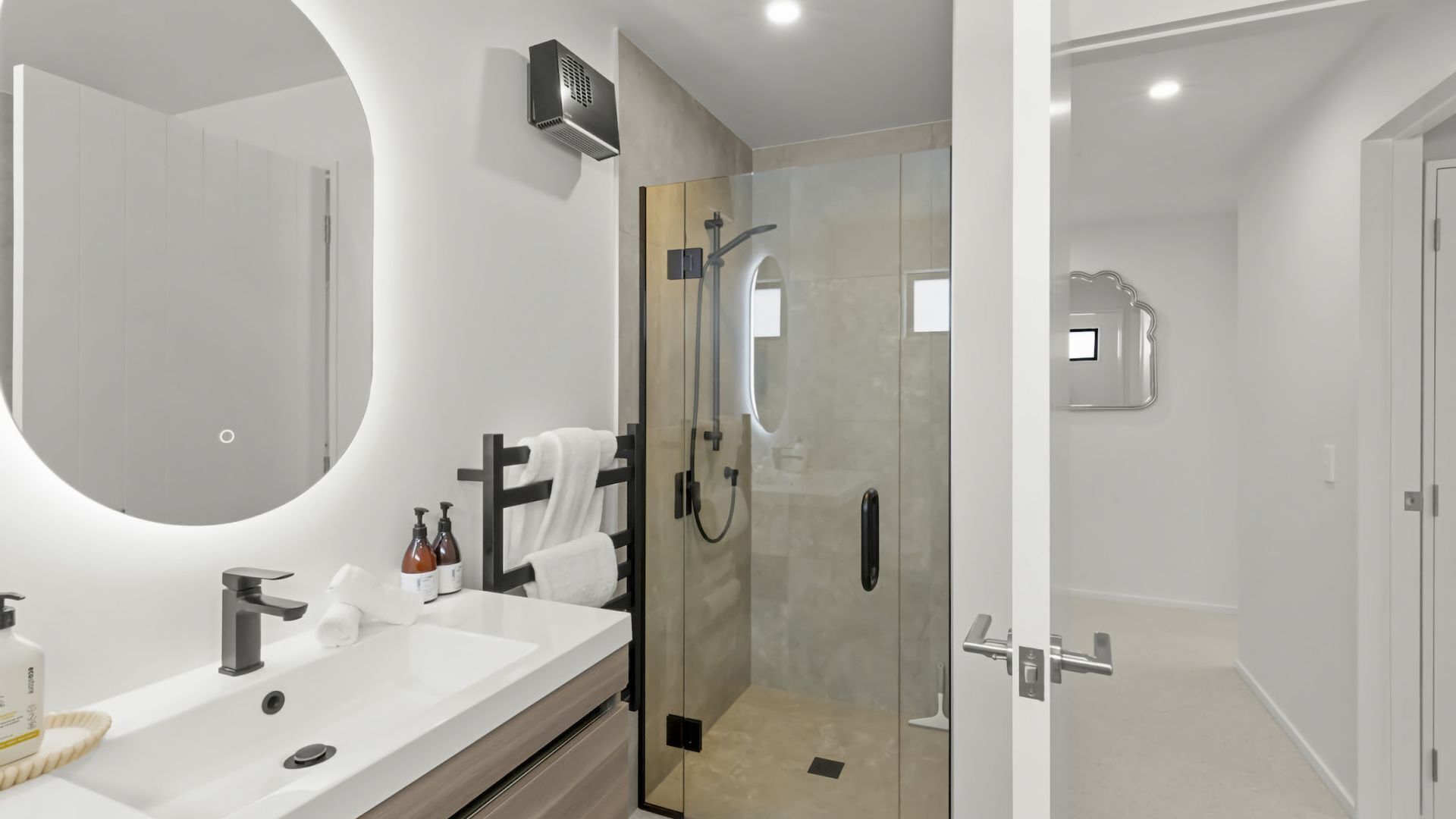 Un baño moderno con un espejo grande, cabina de ducha y tocador con lavabo y artículos de aseo.