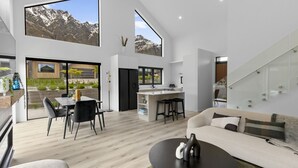 A modern kitchen with a central island, a dining area with a table and chairs, and a living area with a sofa and coffee table. - Marvellous on Muster - family home, mountain views (Jacks Point)
