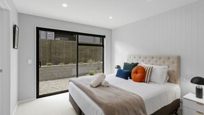 A modern bedroom with a large bed, a nightstand, and a view of a garden through a sliding door. - Marvellous on Muster - family home, mountain views (Jacks Point)
