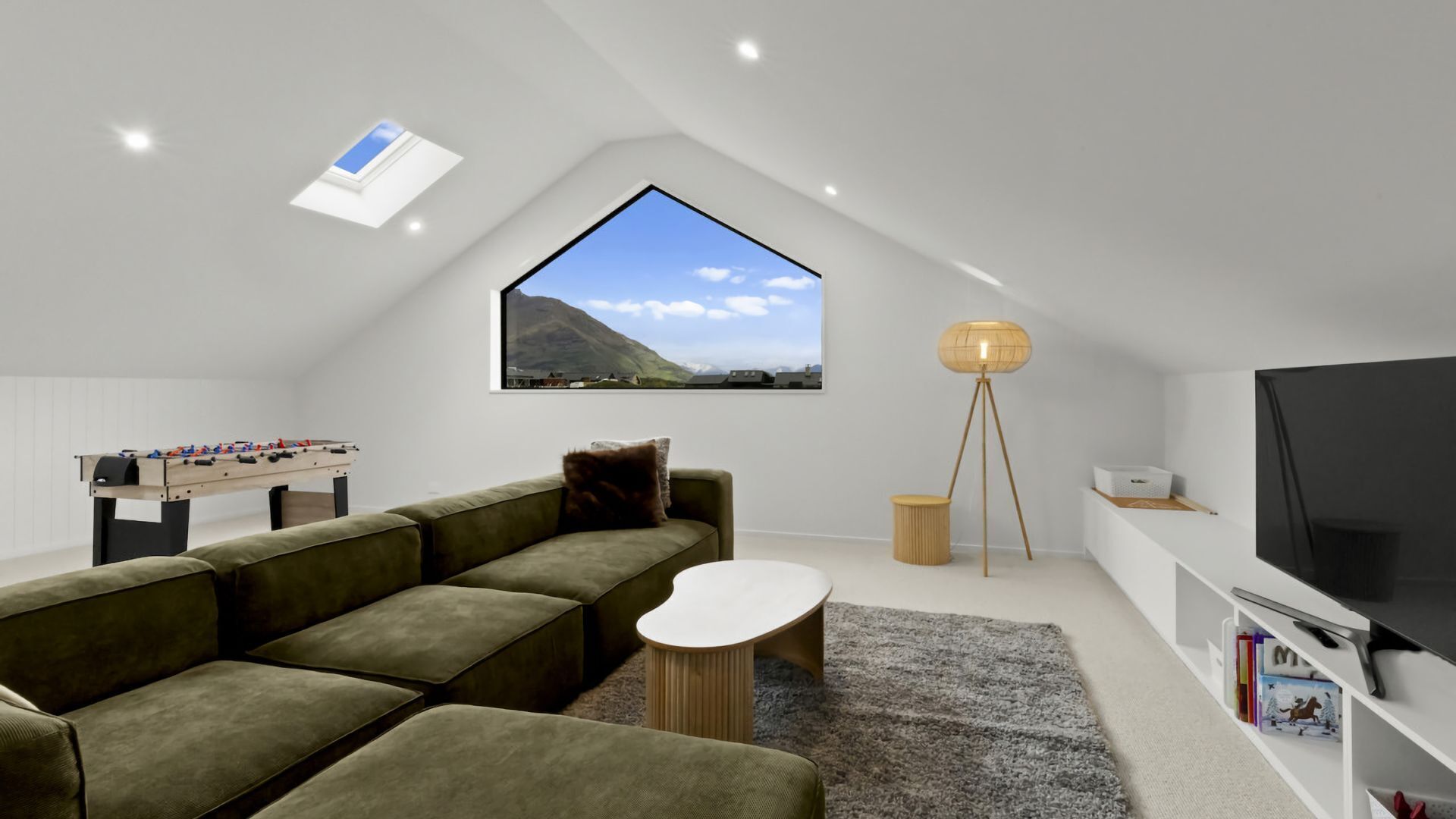 Quarto moderno estilo loft com uma janela grande, um sofá, uma mesinha, um abajur, uma TV e uma mesa de pebolim.