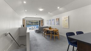 A modern interior with a dining area, a sofa, and a view of a lake. - Alpine Village 23 - 2 bed with lake views (Queenstown)
